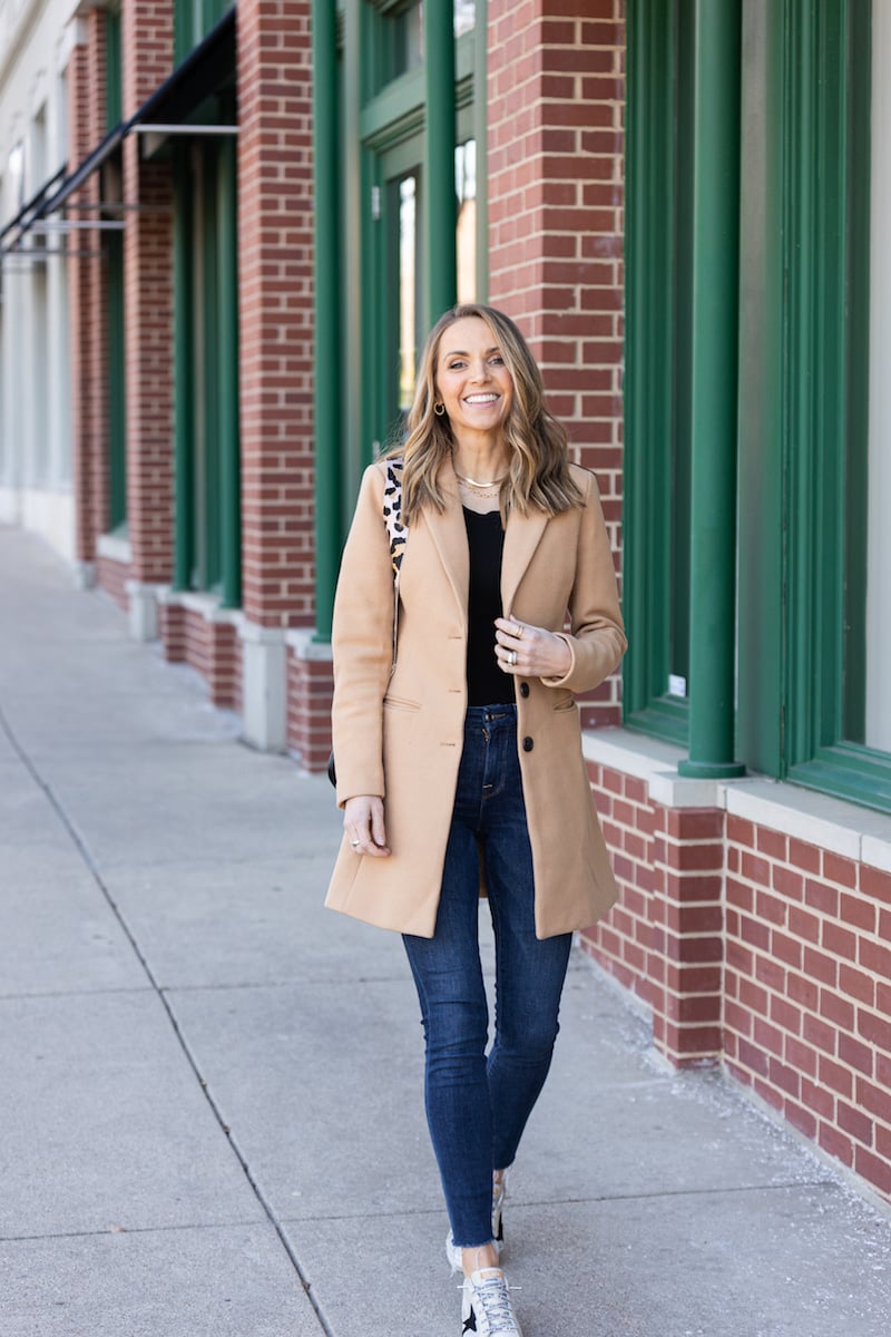 tan coat with blue jeans and black top