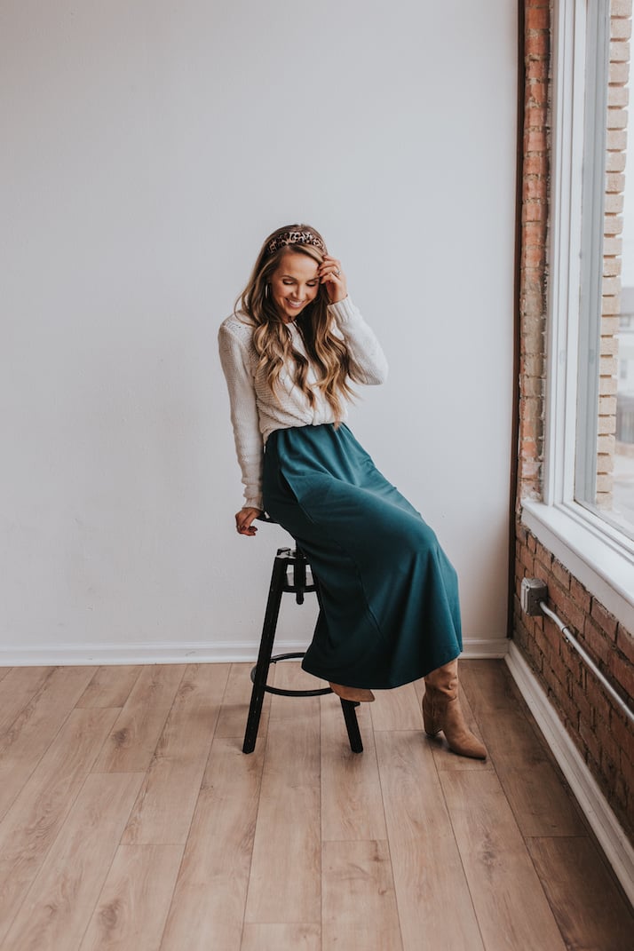 teal dress worn as a skirt with cream cable knit sweater and slouchy boots