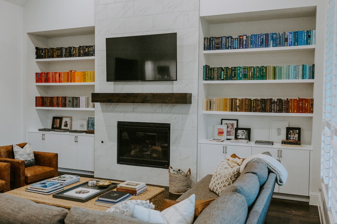 rainbow bookshelf in white floating shelves with marble fireplace